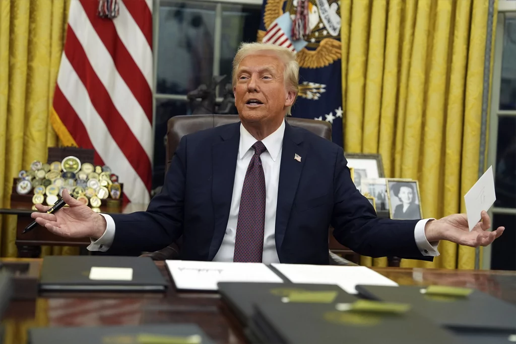 President Donald Trump holds up the letter that former President Joe Biden left for him in the desk as he signs executive orders in the Oval Office of the White House, Monday, Jan. 20, 2025, in Washington. (AP Photo/Evan Vucci)