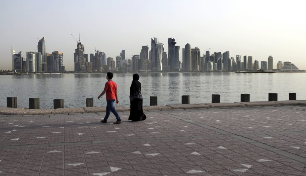 In this Friday, May 4, 2018, photo, a couple walk by the sea with the city skyline in the background, in Doha, Qatar. The diplomatic crisis gripping the energy-rich country of Qatar, the worst to grip the Gulf region since Iraq's 1990 invasion of Kuwait, will turn a year-old on June 5. 