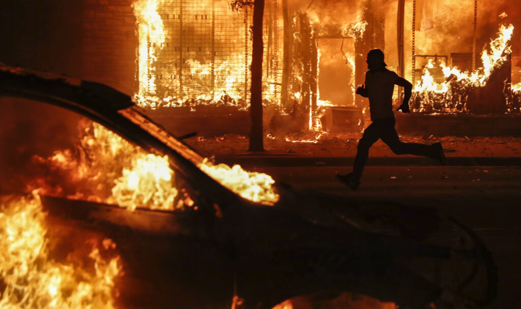 A protester runs past burning cars and buildings on Chicago Avenue, Saturday, May 30, 2020, in St. Paul, Minn. Protests continued following the death of George Floyd, who died after being restrained by Minneapolis police officers on Memorial Day. (AP Photo/John Minchillo)