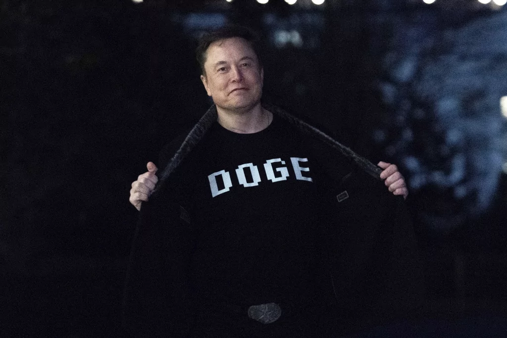 Elon Musk flashes his t-shirt that reads "DOGE" to the media as he walks on South Lawn of the White House, in Washington, Sunday, March 9, 2025.