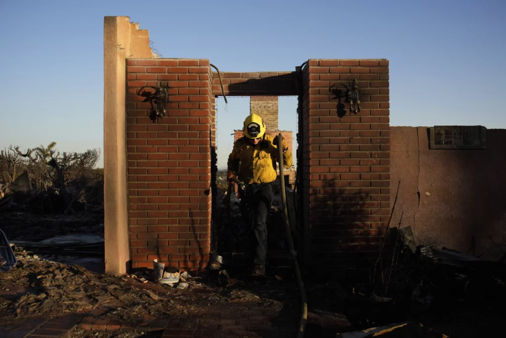 Apple Valley Fire District firefighter Wyatt Cortez walks through a destroyed house as he puts out hotspots from the Palisades fire in the Pacific Palisades neighborhood of Los Angeles, Monday, Jan. 13, 2025. (AP Photo/John Locher)