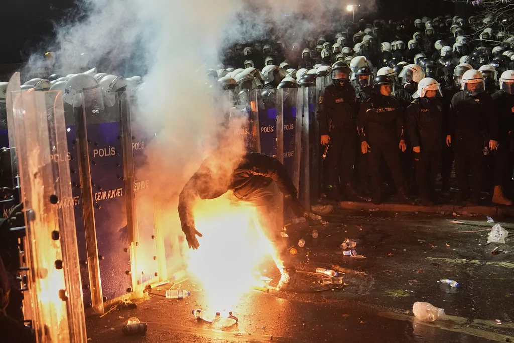 A protester holds a flare next to riot police officers during a protest against the arrest of Istanbul Mayor Ekrem Imamoglu, in Istanbul, Turkey, Saturday, March 22, 2025. 