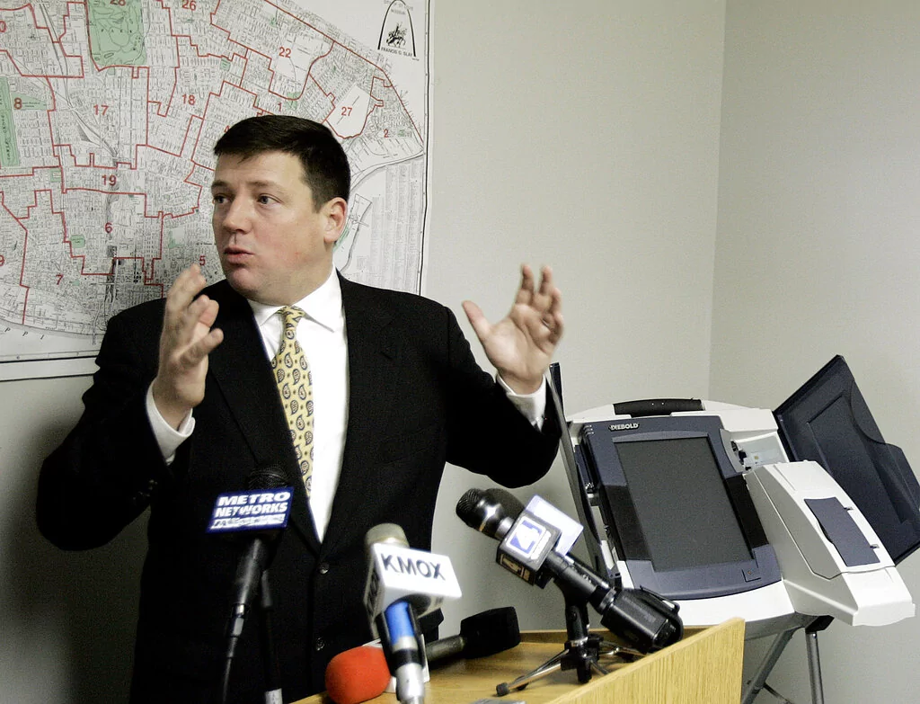 Ed Martin, chairman of the St. Louis Board of Elections, speaks during a news conference, Tuesday, Feb. 21, 2006, in St. Louis, where it was announced the city would use touch-screens, examples seen at right, and optical scan machines for voters to vote. Absentee voters for the April 4 municipal election began using touch-screen ballot boxes on Tuesday. Officials said the historically low turnout during the April election will make that a perfect testing ground to work out bugs before the machines go into wider use. 