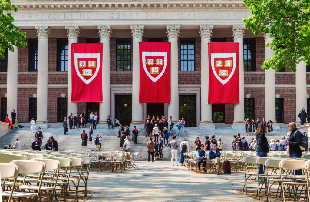 Cambridge, Massachusetts — May 22, 2023: Students in graduation gowns and families in front of the Harry Elkins Widener Memorial Library. Harvard VERITAS banners hang in front of building. The library houses some 3.5 million books in its stacks and is the centerpiece of the Harvard College Libraries. It honors 1907 Harvard College graduate and book collector Harry Elkins Widener.
