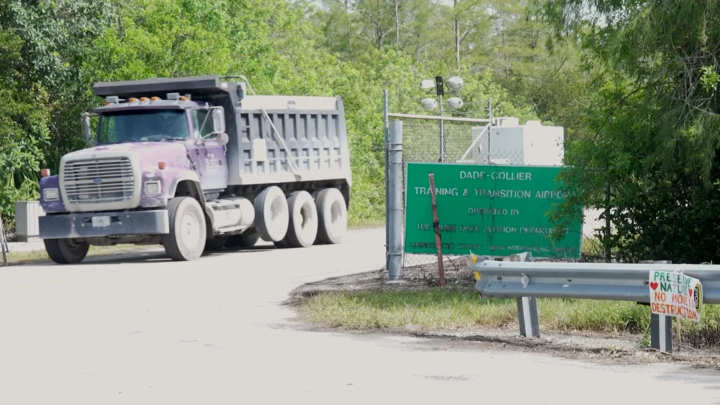 Dump truck next to a fence with a green sign on it.