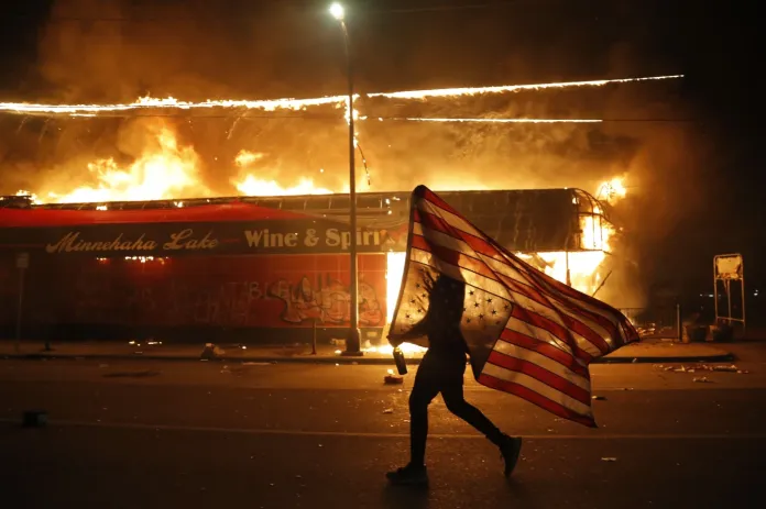 In this May 28, 2020, file photo, a protester carries an American flag upside down, a sign of distress, next to a burning building in Minneapolis. (AP Photo/Julio Cortez, File)