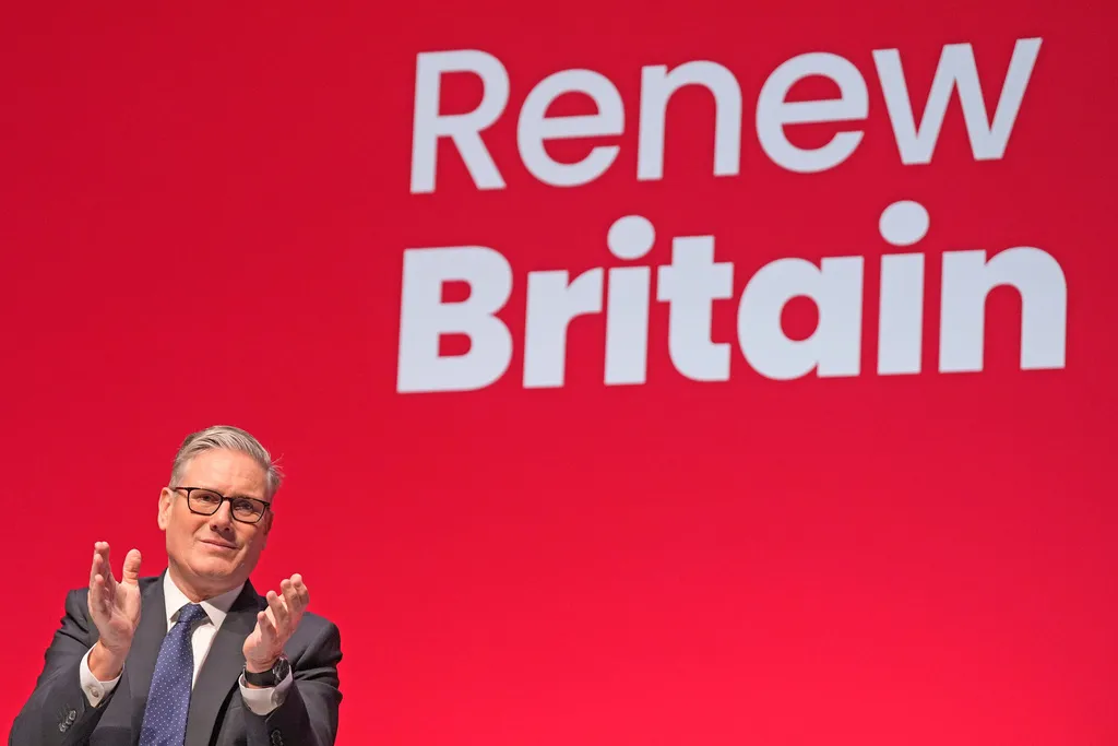 U.K. Prime Minister Keir Starmer claps in front of a red "Renew Britain" sign.