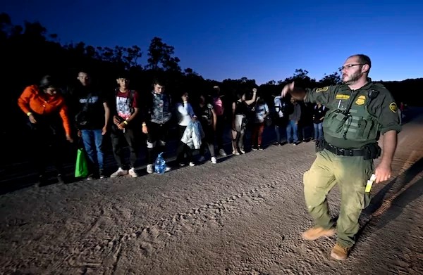 A U.S. Border Patrol agent processes asylum-seekers from Peru after they crossed the nearby border with Mexico, Tuesday Sept. 26, 2023, near Jacumba Hot Springs, California. Migrants continue to arrive to desert campsites along California's border with Mexico, as they await processing. (AP Photo/Denis Poroy)