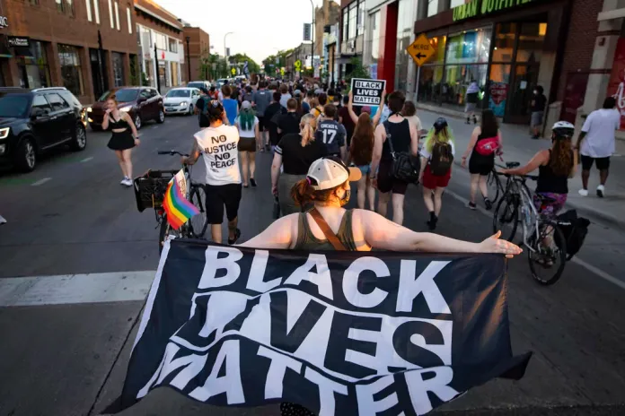 A woman holds a Black Lives Matter flag as community members march, Sunday, June 6, 2021, in Minneapolis.