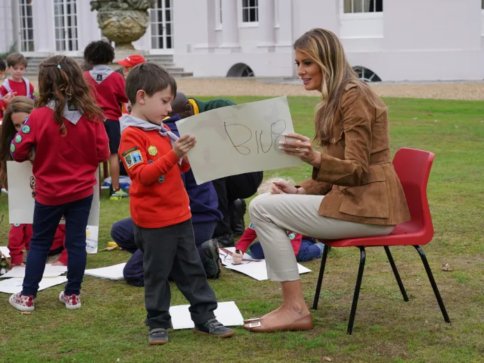 First lady Melania Trump sits in a chair as she looks at a child's artwork.