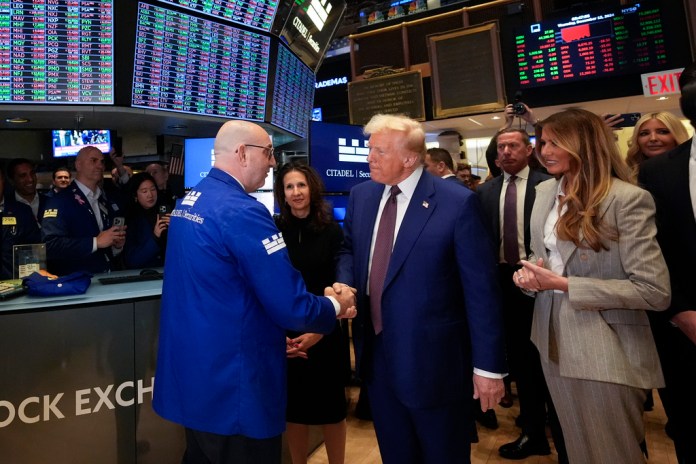 President Donald Trump, with Lynn Martin, President NYSE, center, and Melania Trump, right, is greeted by trader Peter Giacchi, as he walks the floor of the New York Stock Exchange, Thursday, Dec. 12, 2024, in New York. (AP Photo/Alex Brandon)