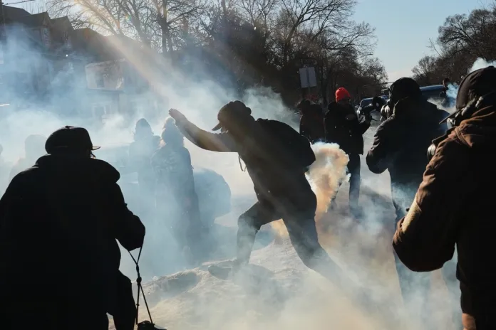 A protester runs through the tear gas near the scene where Renee Good was fatally shot by an ICE officer last week, Tuesday, Jan. 13, 2026, in Minneapolis.