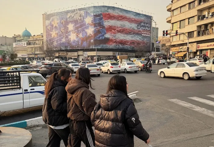 People walk in front of a billboard with a graphic showing a U.S aircraft carrier with damaged fighter jets on its deck, and sign reading in Farsi and English: "If you sow the wind, you'll reap whirlwind," at the Enqelab-e-Eslami (Islamic Revolution) square, in Tehran, Iran, Sunday, Jan. 25, 2026. (AP Photo/Vahid Salemi)