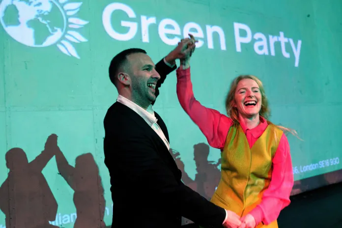 Hannah Spencer celebrates in front of a screen displaying the Green Party logo