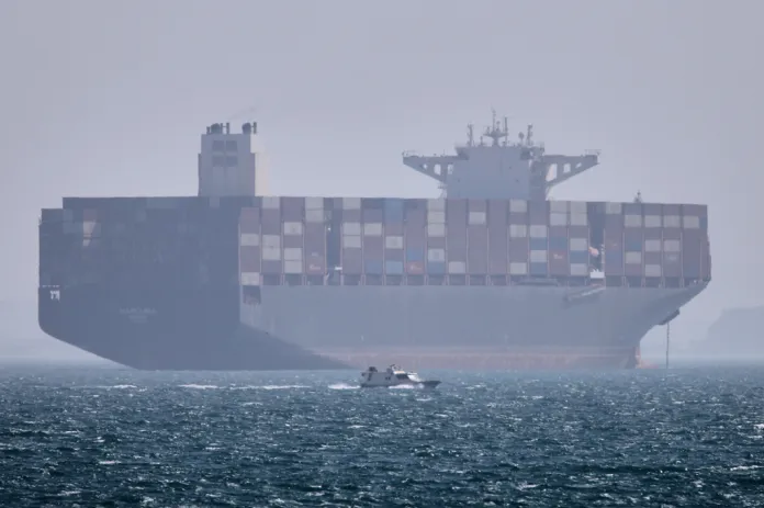 A container ship sits at anchor as a small motorboat passes in the foreground in the Strait of Hormuz off Bandar Abbas, Iran, Saturday, May 2, 2026. (Amirhosein Khorgooi/ISNA via AP)