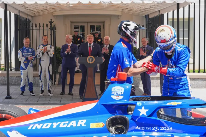 David Malukas, right, exits a race car as Felix Rosenqvist, Alex Palou, Bud Denker, Donald Trump, Roger Penske, and Eric Shanks watch